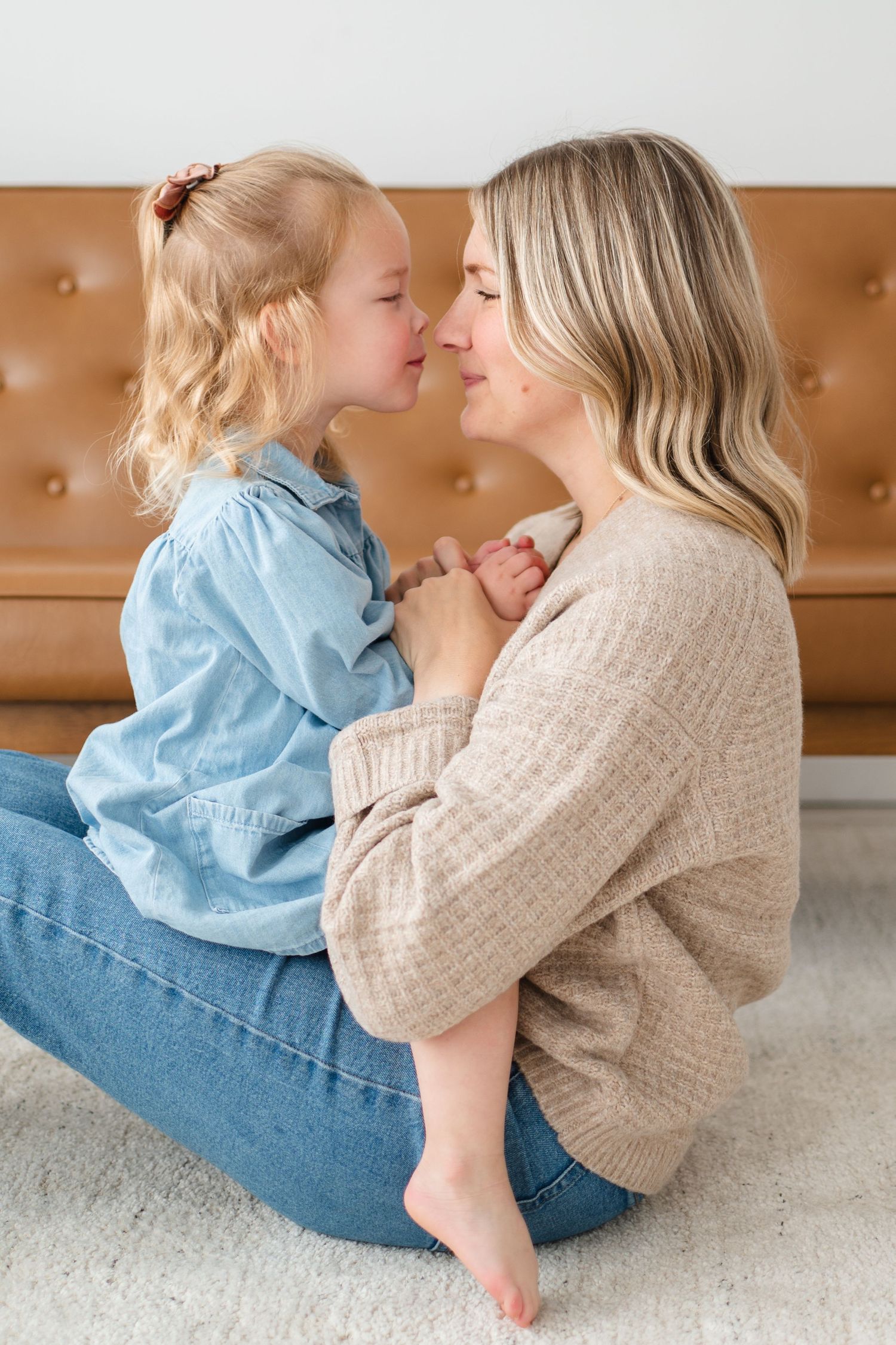 A tender moment shared between parent and child as they sit together on a carpeted floor against a brown sofa.