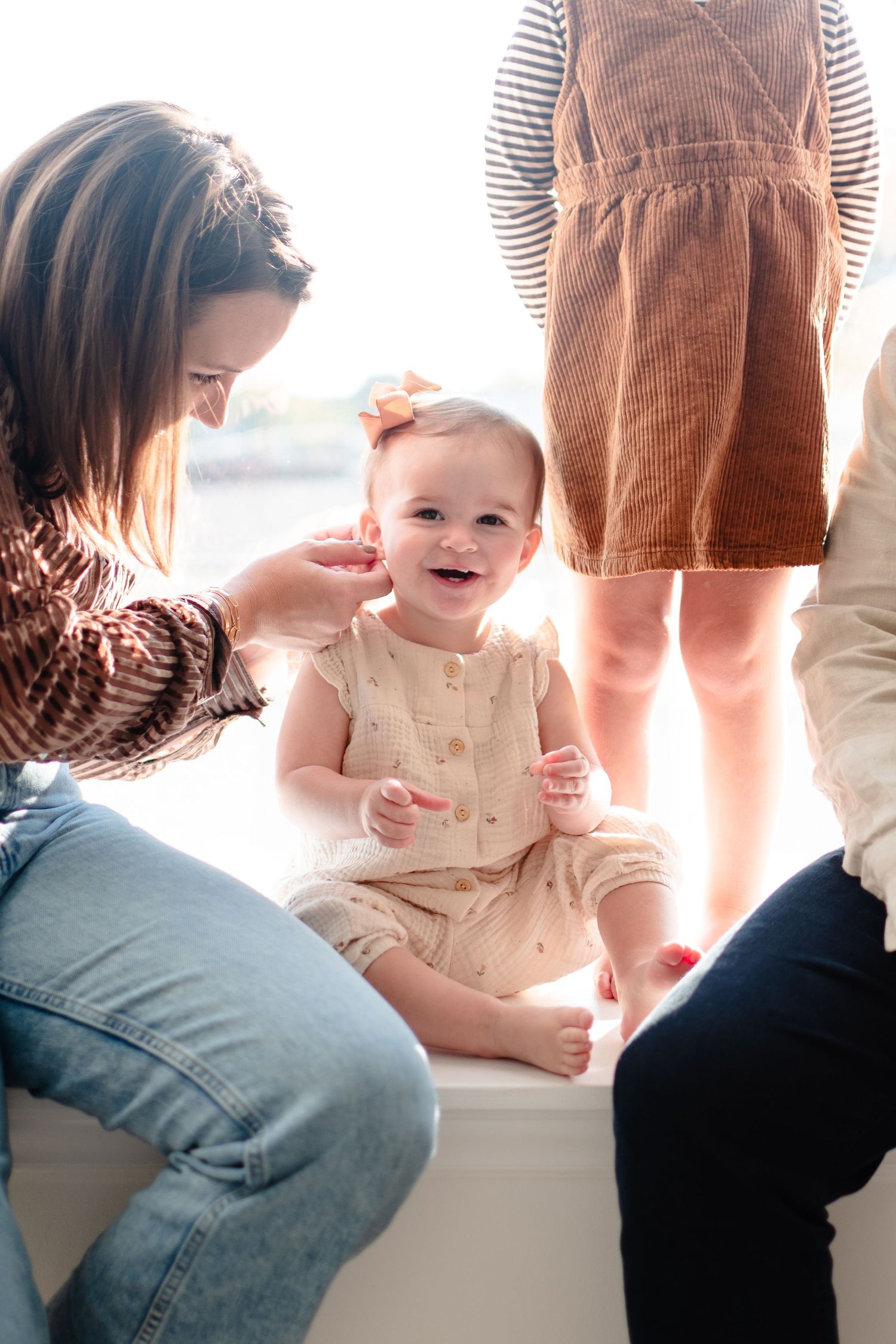 Two adults and a toddler sitting at a window ledge in casual clothing during a bright sunny day.