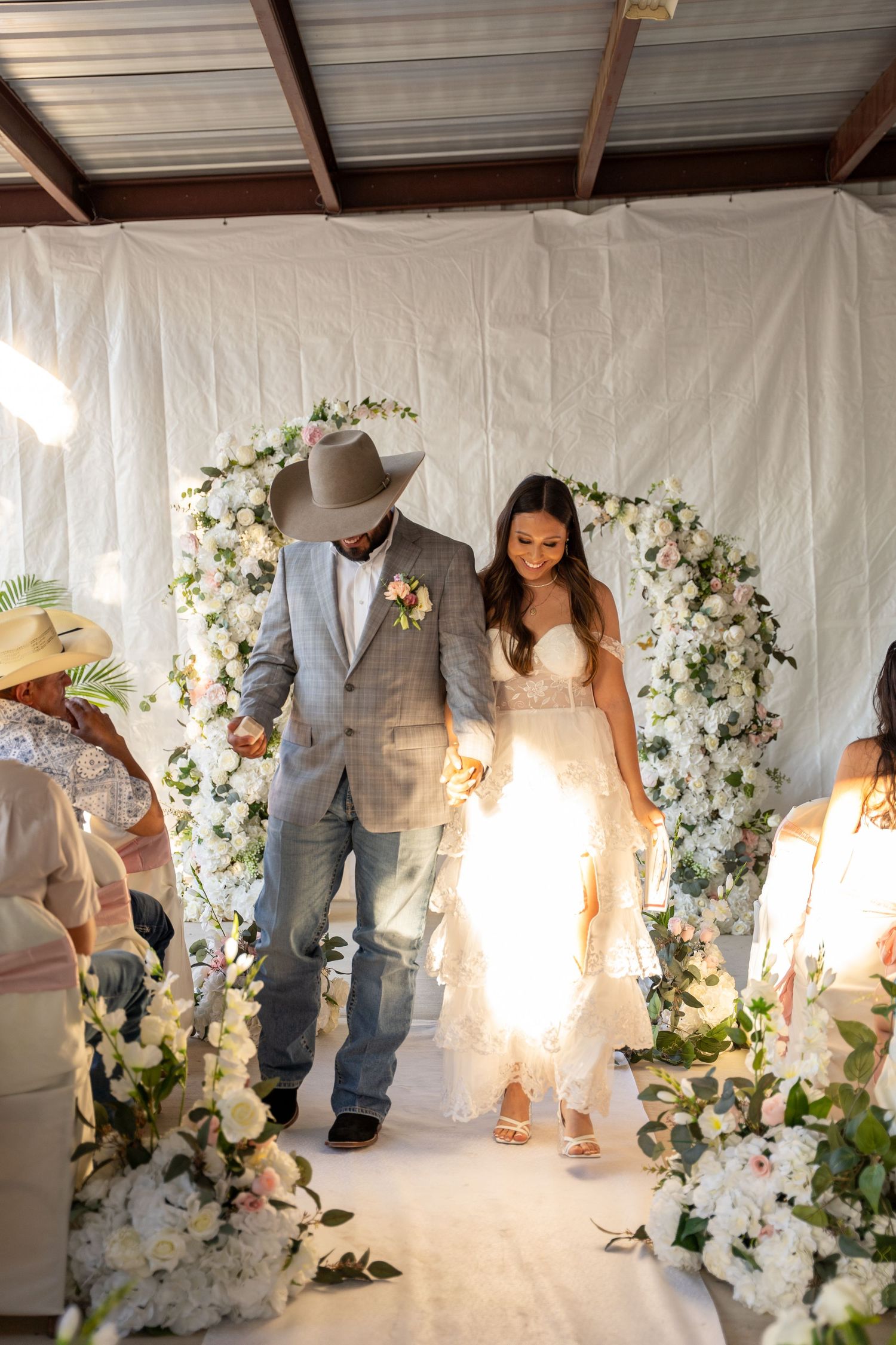 Wedding ceremony under floral arch with white flowers and greenery.