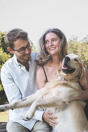 Happy couple outdoors with their friendly golden Labrador retriever dog on a sunny day.