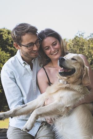 A happy couple plays and cuddles with their golden retriever dog outdoors in the park on a sunny afternoon.