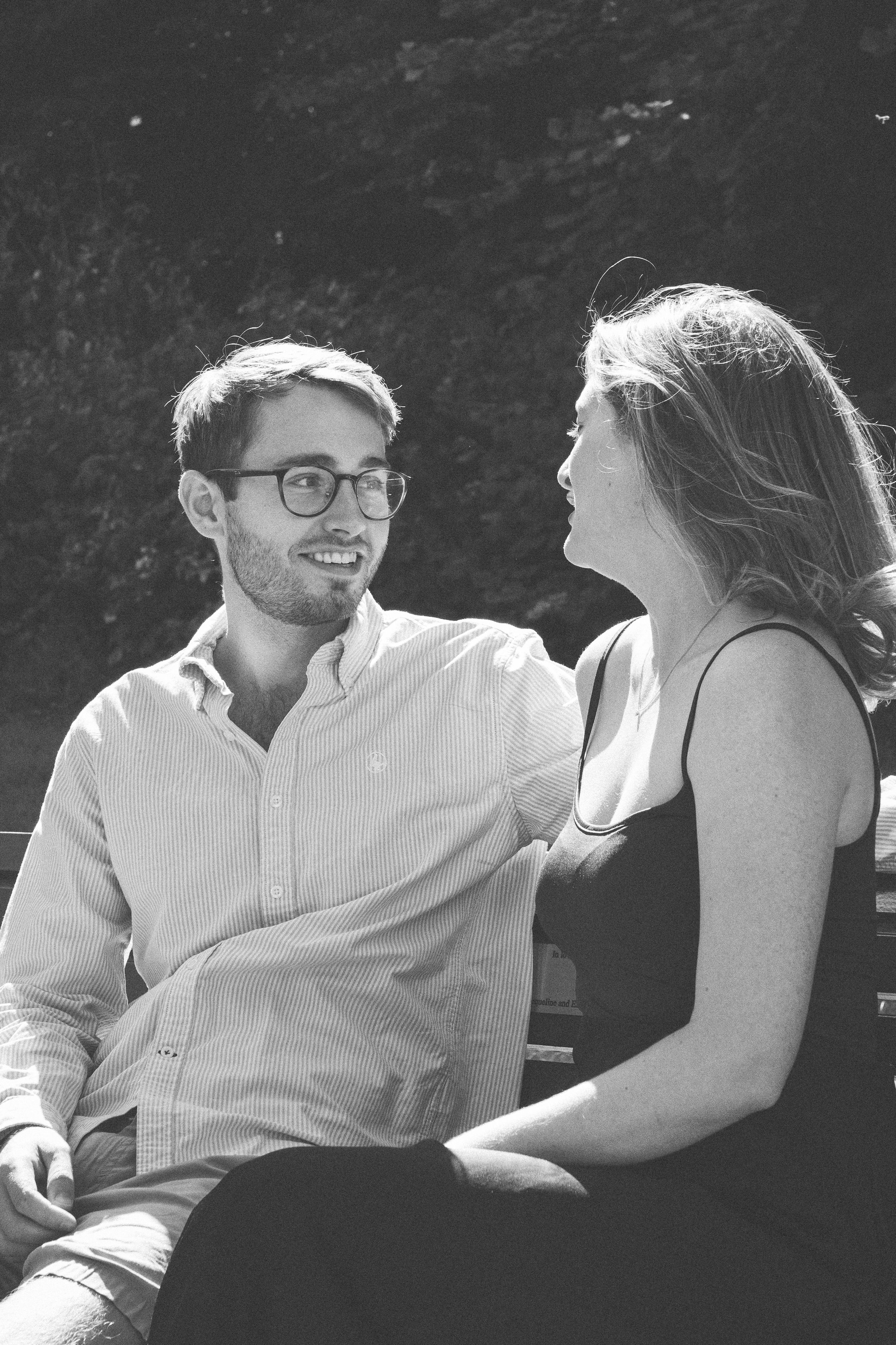 A candid black and white portrait of a couple sharing a tender moment while sitting together outdoors.