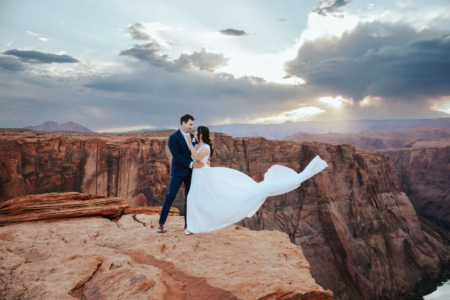 Couple taking romantic photos on the edge of a dramatic red rock canyon cliff during sunset in Utah.