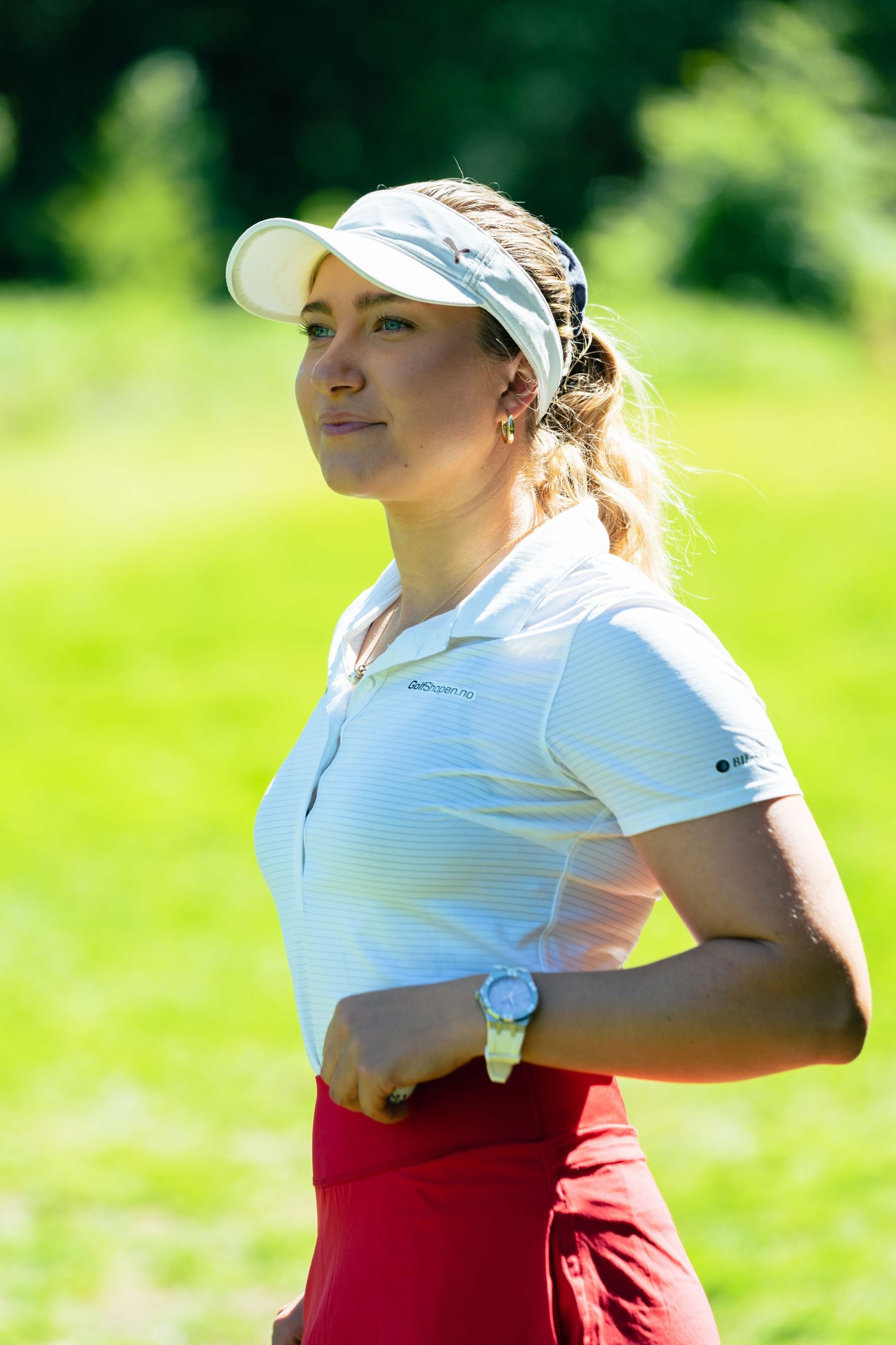 Profesjonell golfspiller i hvit piqué og rød skjørt står på en solrik bane under turneringsspill.