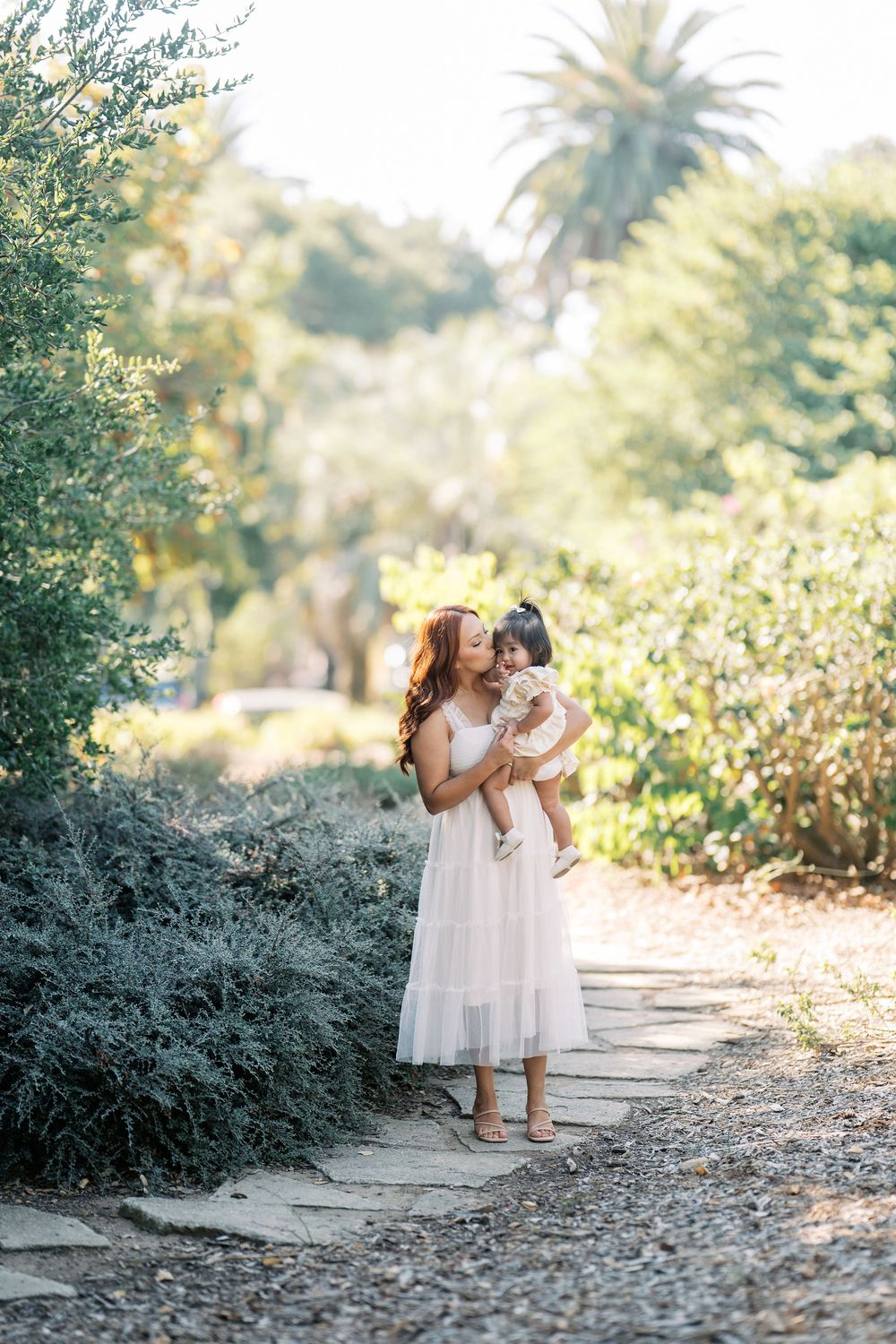 A tender moment captured on a garden path with palm trees and lush greenery in the background.