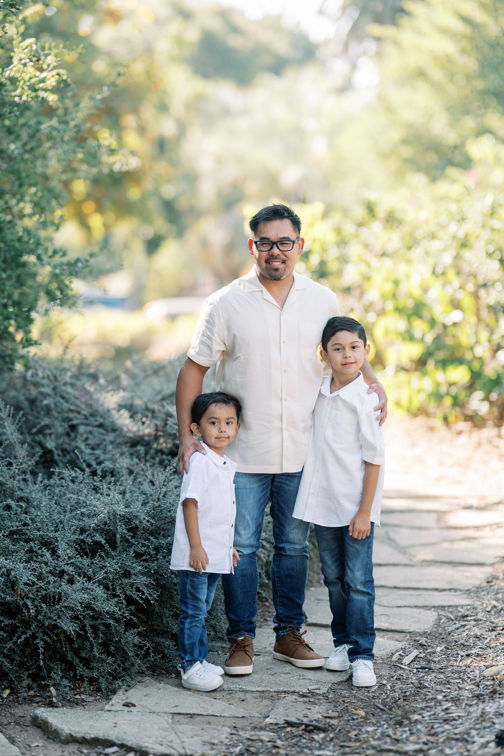 Family members pose together on stone steps surrounded by greenery in coordinated white and denim outfits.
