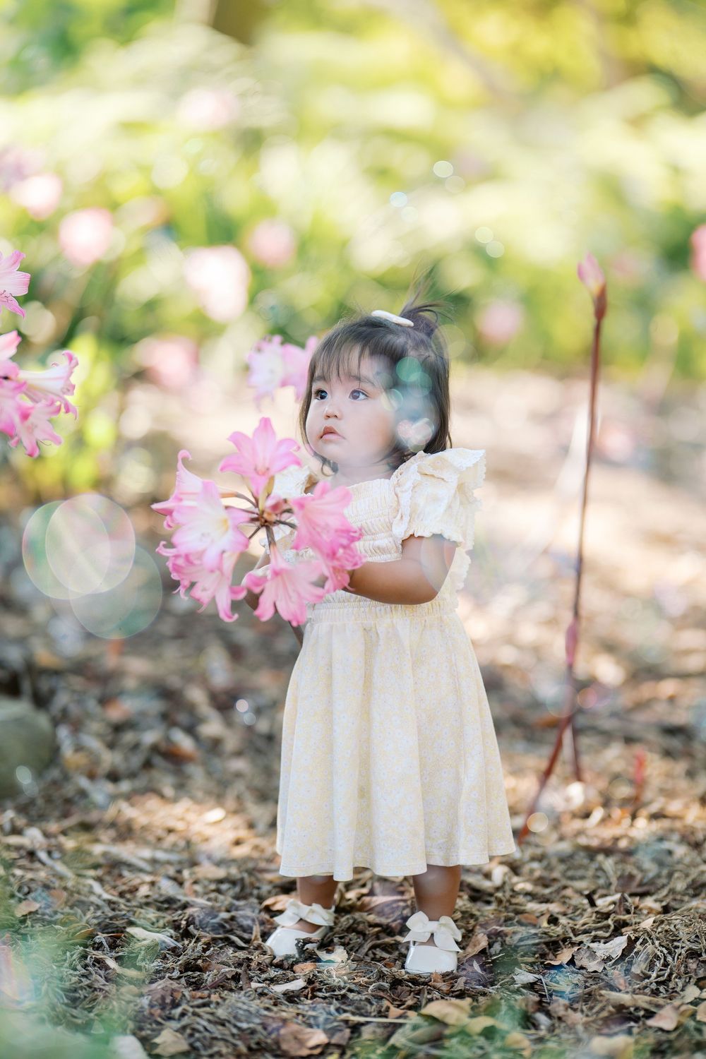 A white dress-clad figure among pink flowers and fallen leaves in a dreamy garden setting.