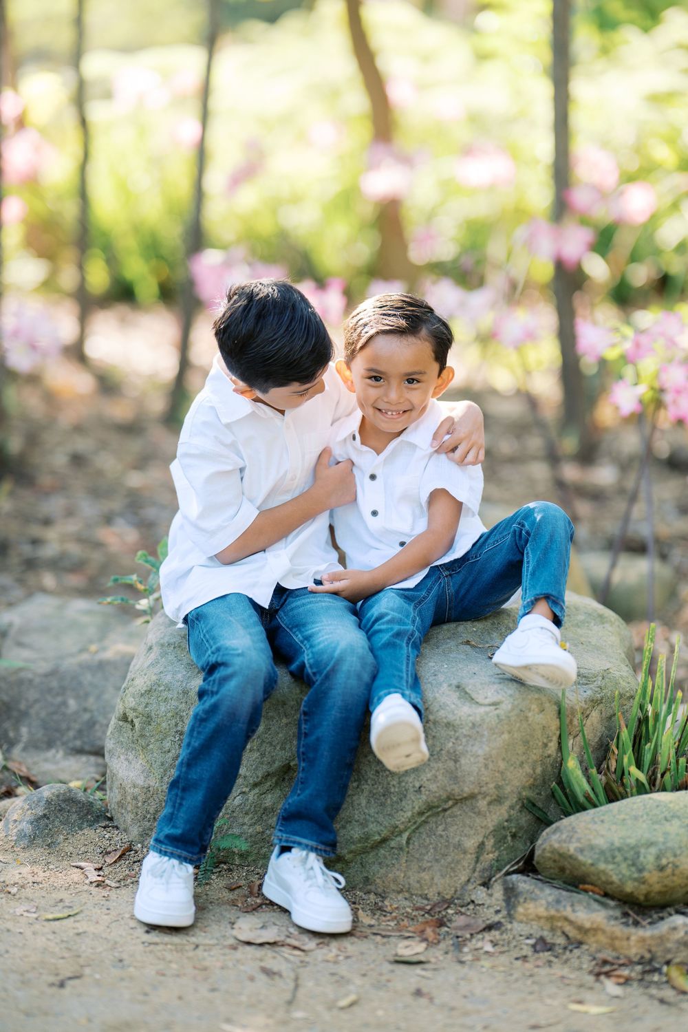 Two people sharing a tender moment while sitting on large rocks in a blooming garden.
