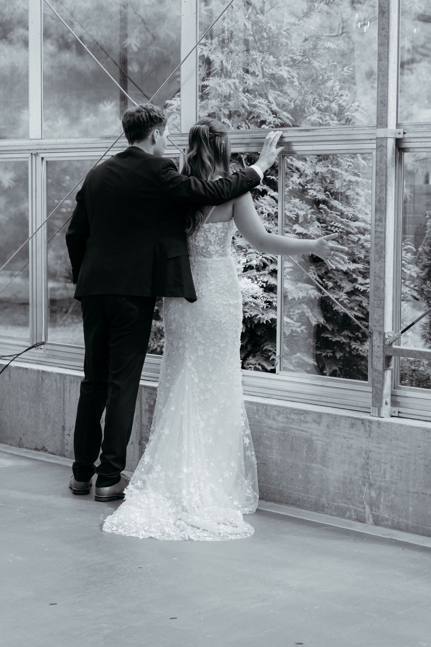 Black and white wedding photo showing couple looking through glass-enclosed space. The Ivy House Greenhouse in Saugatuck, Michigan