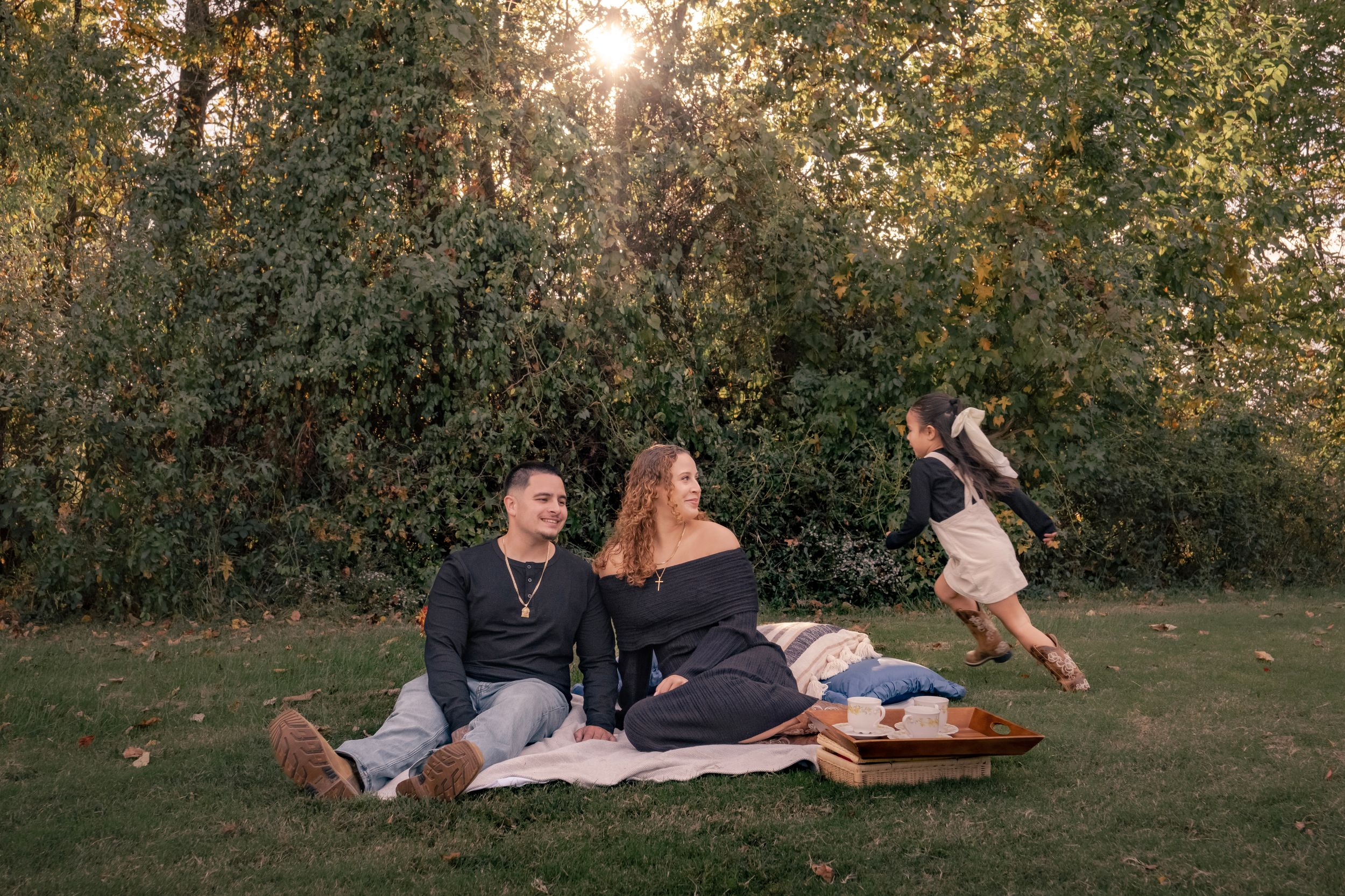 A couple relaxes on a blanket in a sunlit garden during golden hour while enjoying a picnic together.