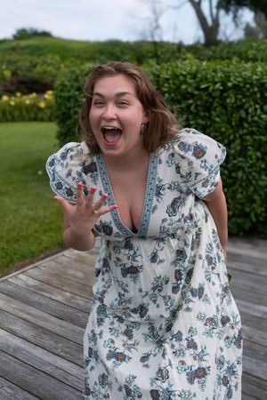 Person in floral dress laughing joyfully on outdoor wooden deck.