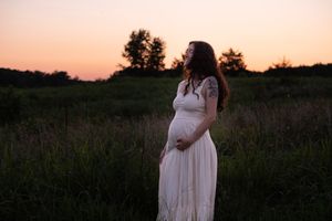 A dreamy maternity photoshoot featuring a flowing white dress against a sunset backdrop in a field.
