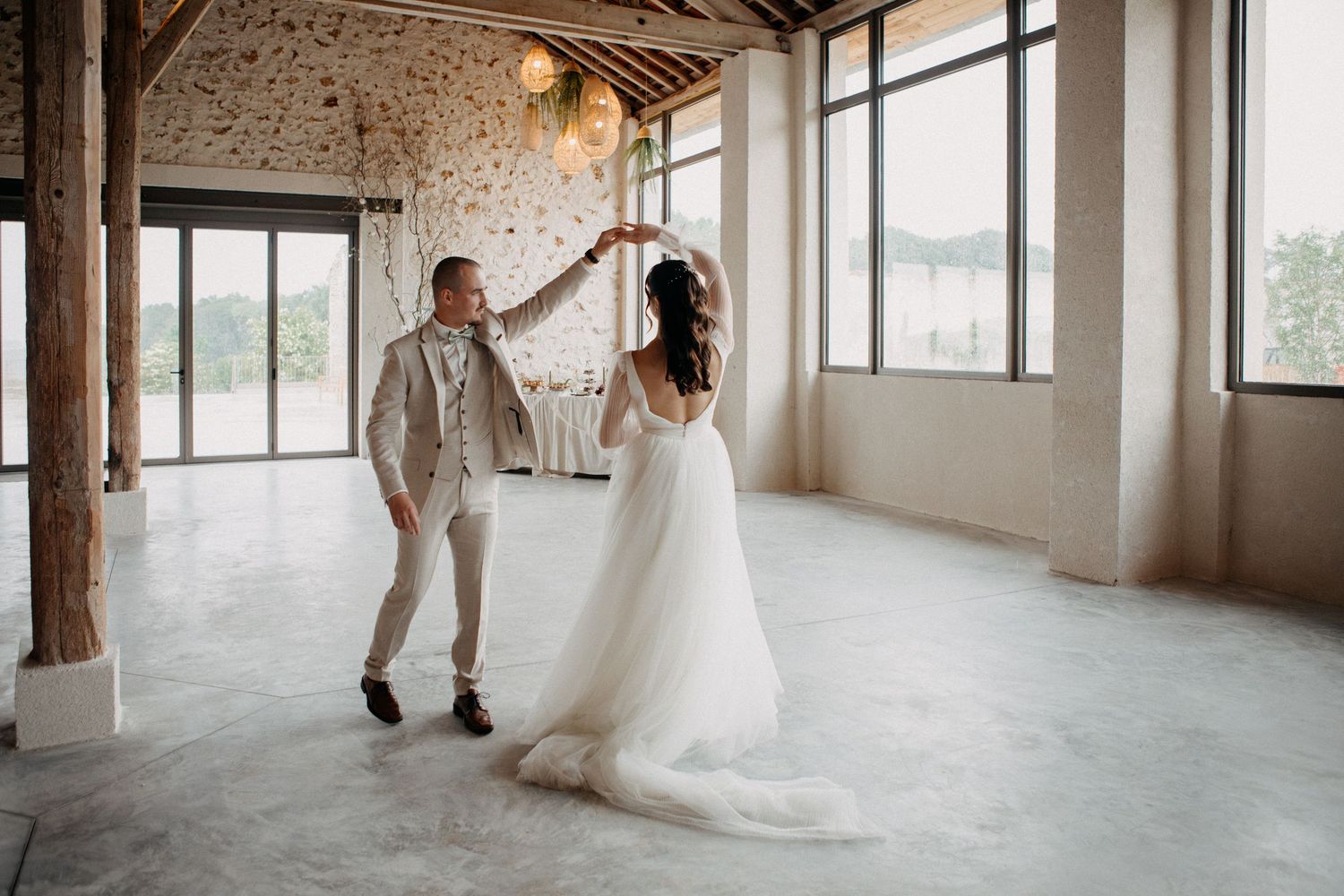 Bride and groom dance together in an airy, sunlit wedding venue with stone walls.