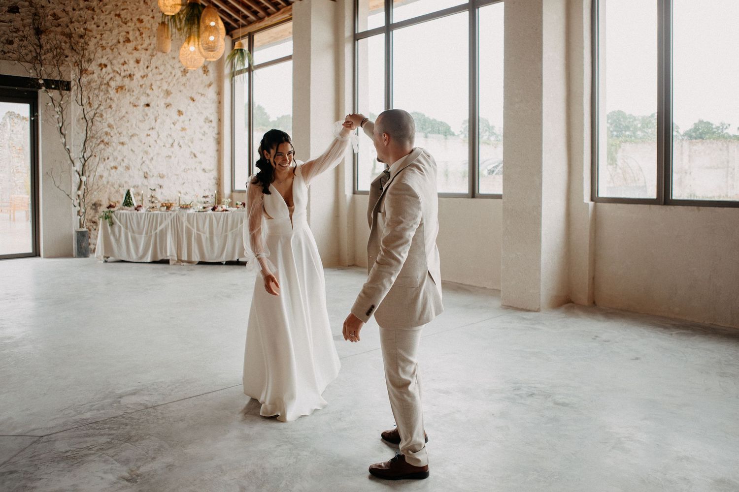 Bride and groom share first dance in a bright, modern wedding venue with large windows.