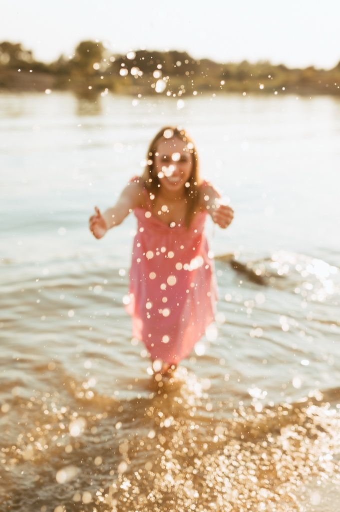 Silhouette of a figure in a pink dress splashing through sun-dappled beach water at golden hour.
