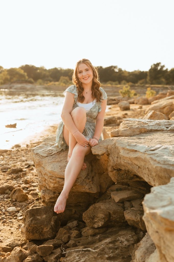 Person sits on coastal rock formations during golden hour at a beach as sunlight creates warm natural lighting.