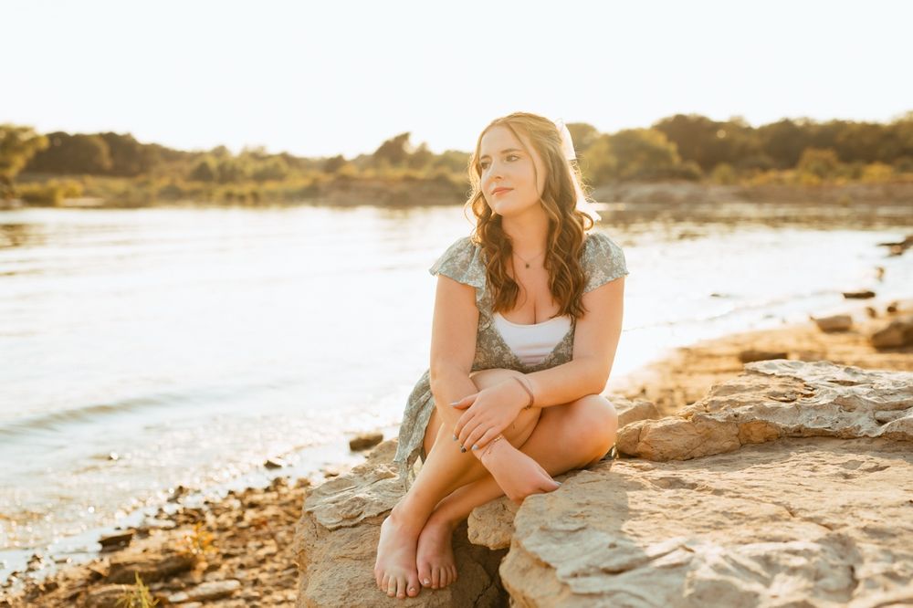 Person in casual summer attire lounges on warm rocks near a golden beach during sunset.