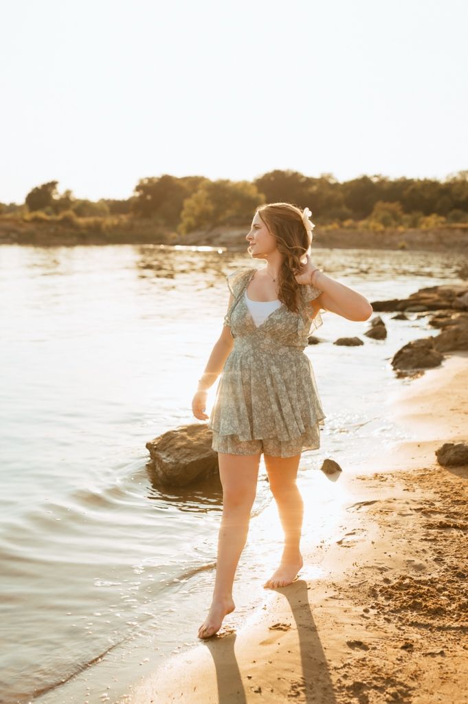 A summery floral dress sparkles in golden sunlight as waves lap at the sandy shoreline during sunset.
