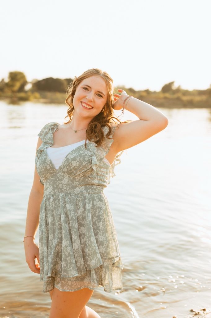 A light and airy photoshoot at sunset featuring a floral dress and soft golden lighting by the water.