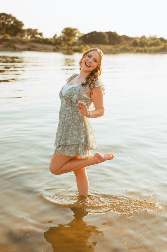 Person in flowy blue dress splashing and playing in shallow water at sunset during golden hour.