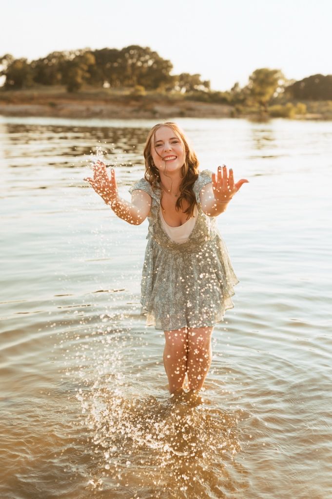 Person splashing and playing in shallow ocean water at sunset creating sparkles and ripples in the golden light.