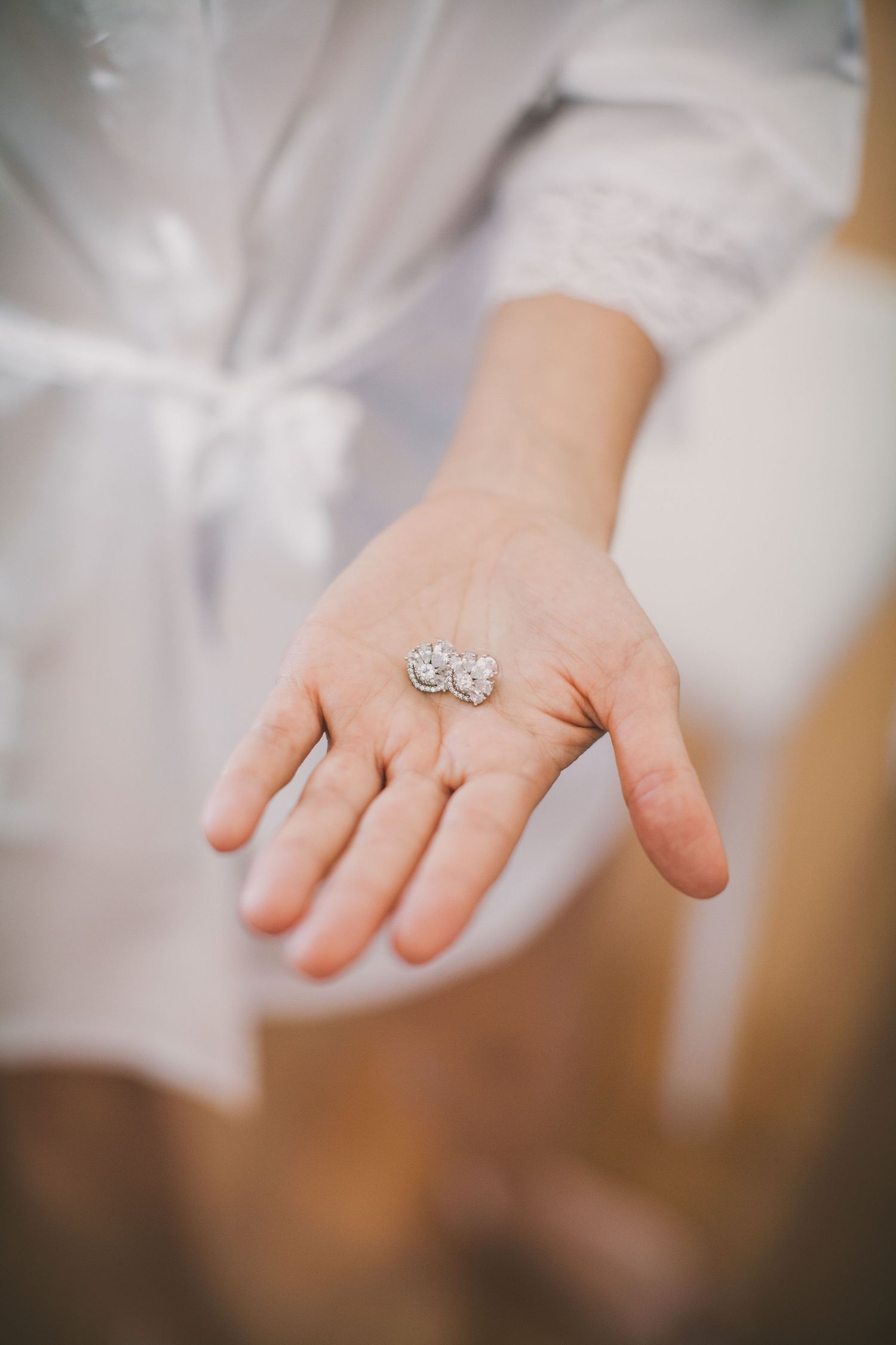 A delicate white lace bridal gown sleeve and hand wearing an ornate vintage-style engagement ring with sparkles.