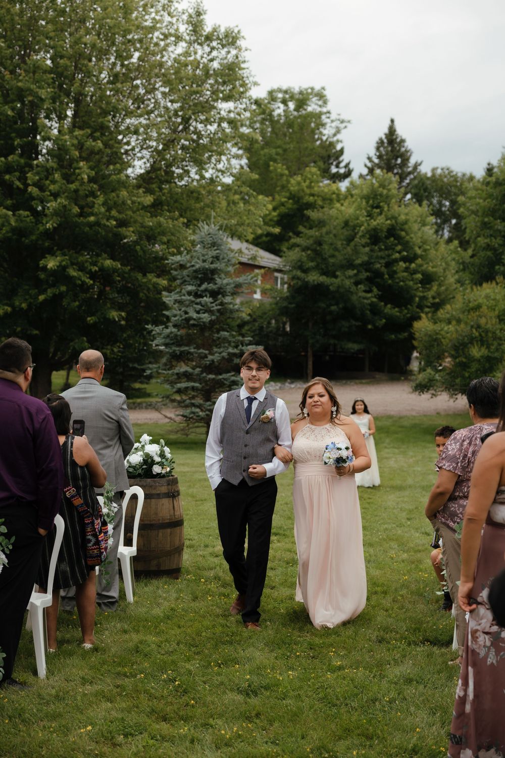 Wedding guests gather on a grassy lawn with white chairs set up for an outdoor ceremony.
