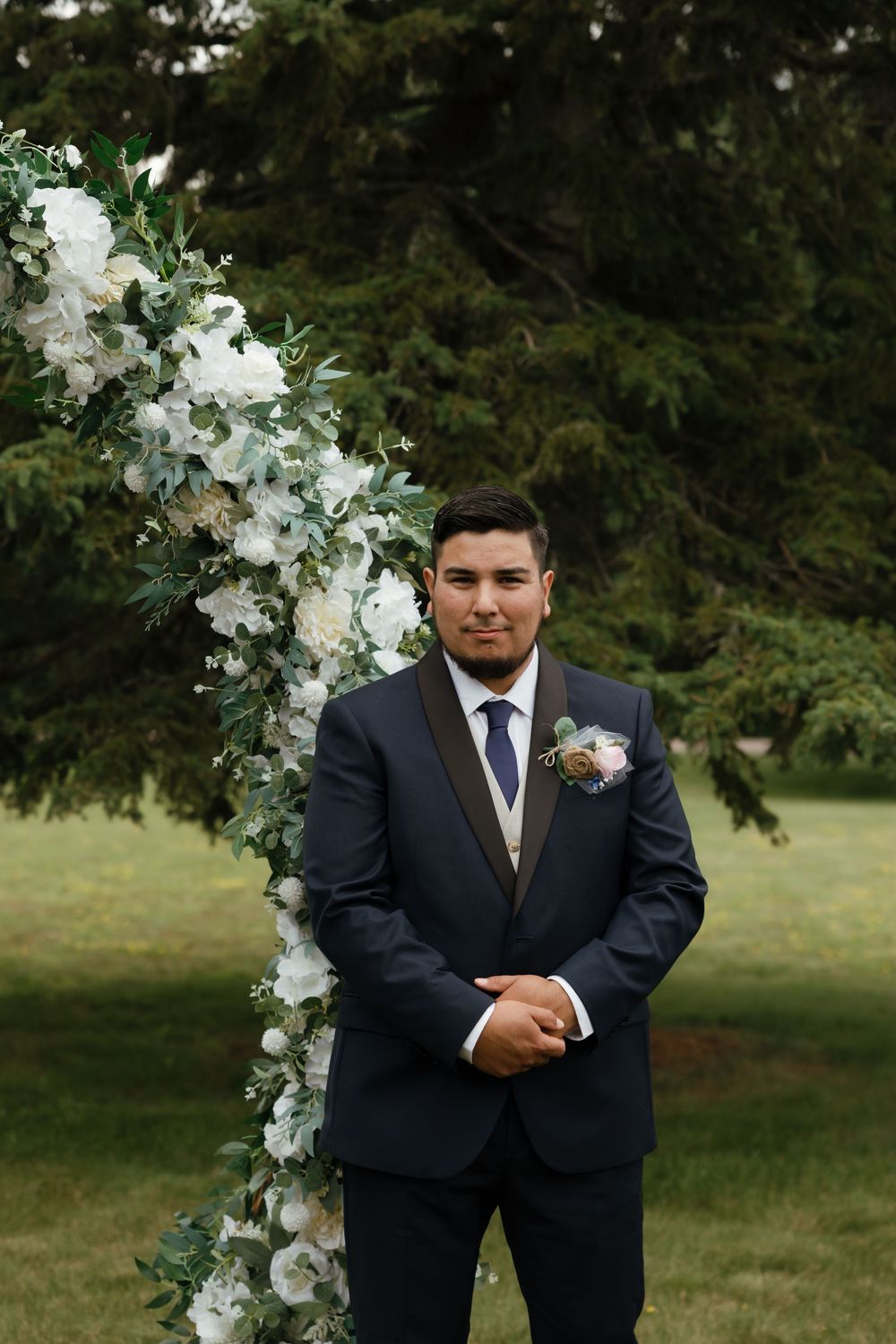 A formal event setup outdoors features a white floral arch with elegant decorations against a natural backdrop.