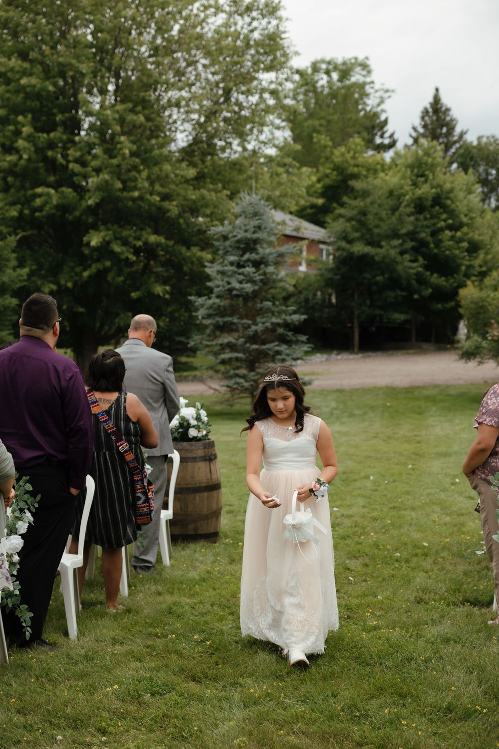 Wedding guests seated in white chairs on a grassy lawn during an outdoor garden ceremony.