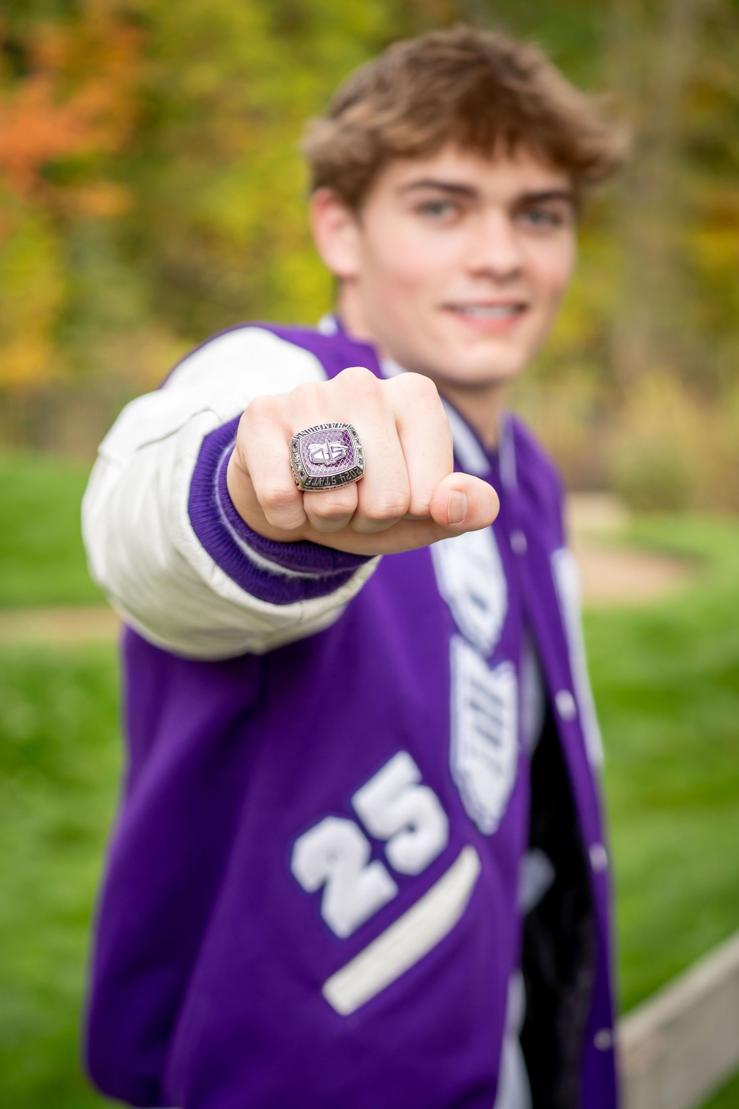 Someone wearing a purple varsity jacket in an outdoor setting showing off their state championship ring.
