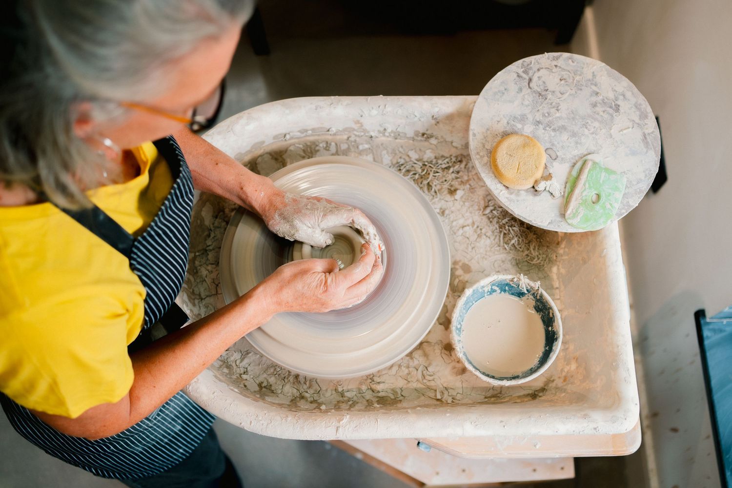 Someone creates delicate lace patterns by pressing a doily pattern into rolled ceramic clay using a rolling pin.