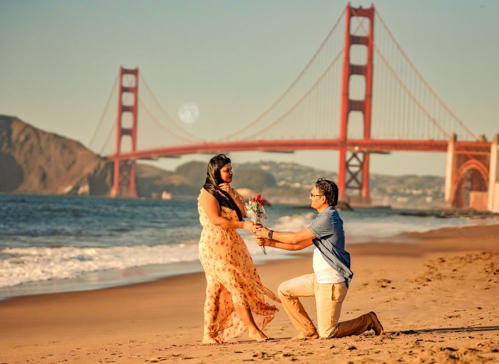Two people share an intimate moment at sunset on Baker Beach with the Golden Gate Bridge in the background.