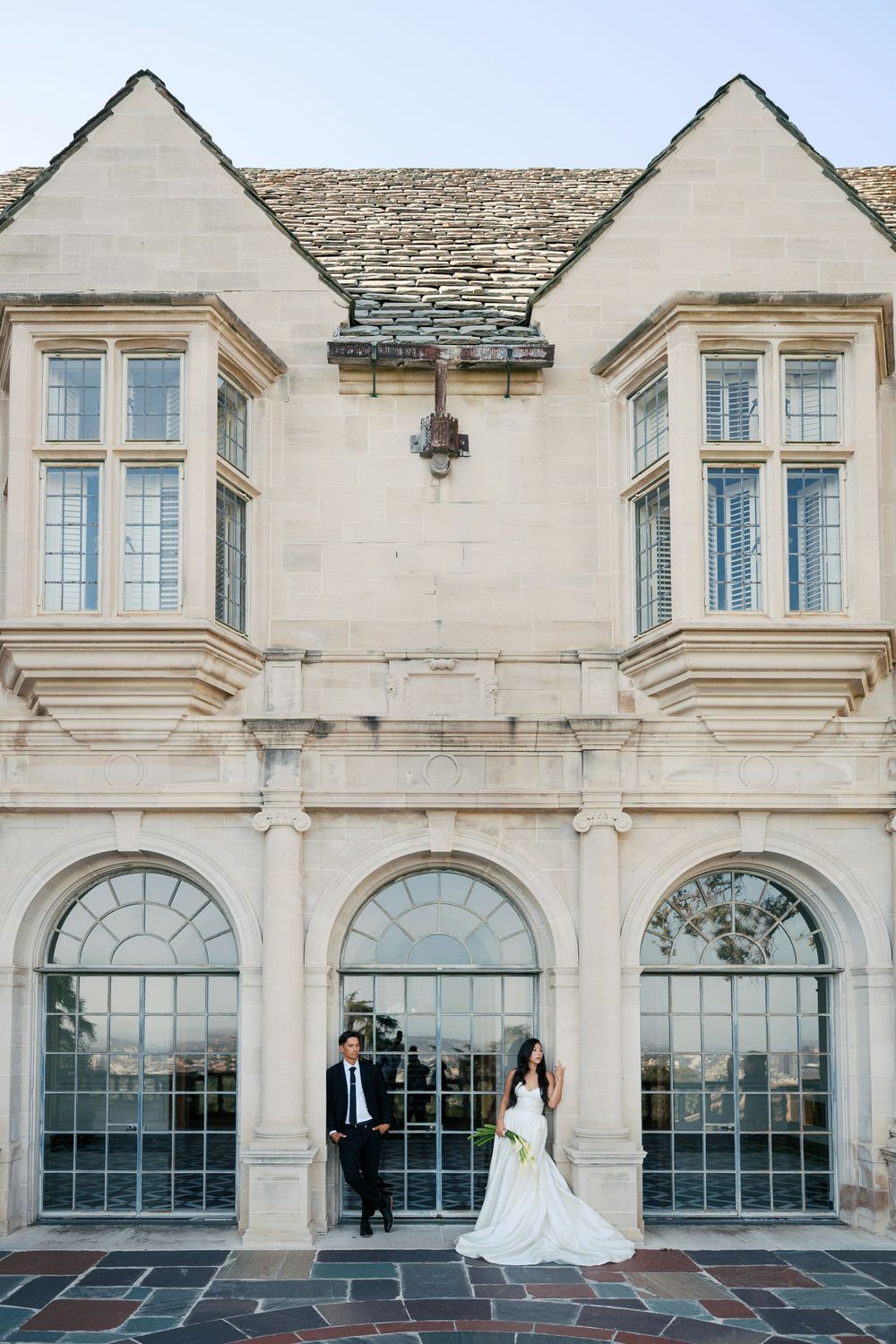 A sequence of wedding portraits taken in front of a classic stone mansion with large arched windows.