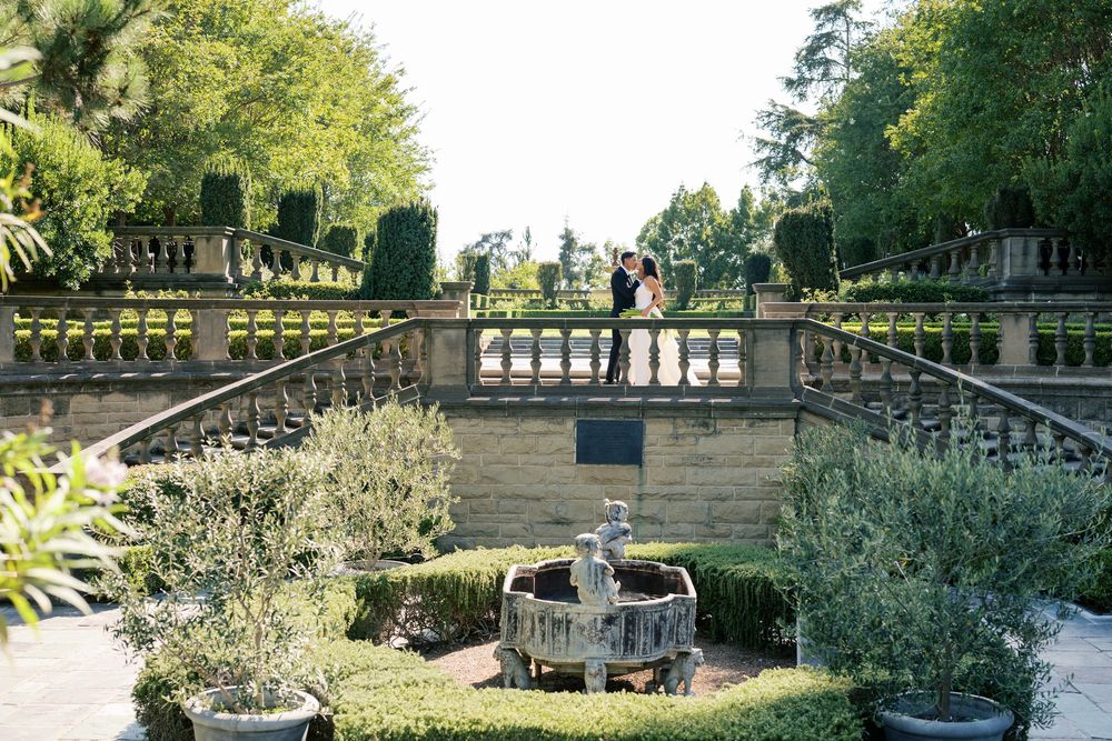 Panoramic view of an ornate stone balustrade and landscaping in a formal garden on a sunny day.