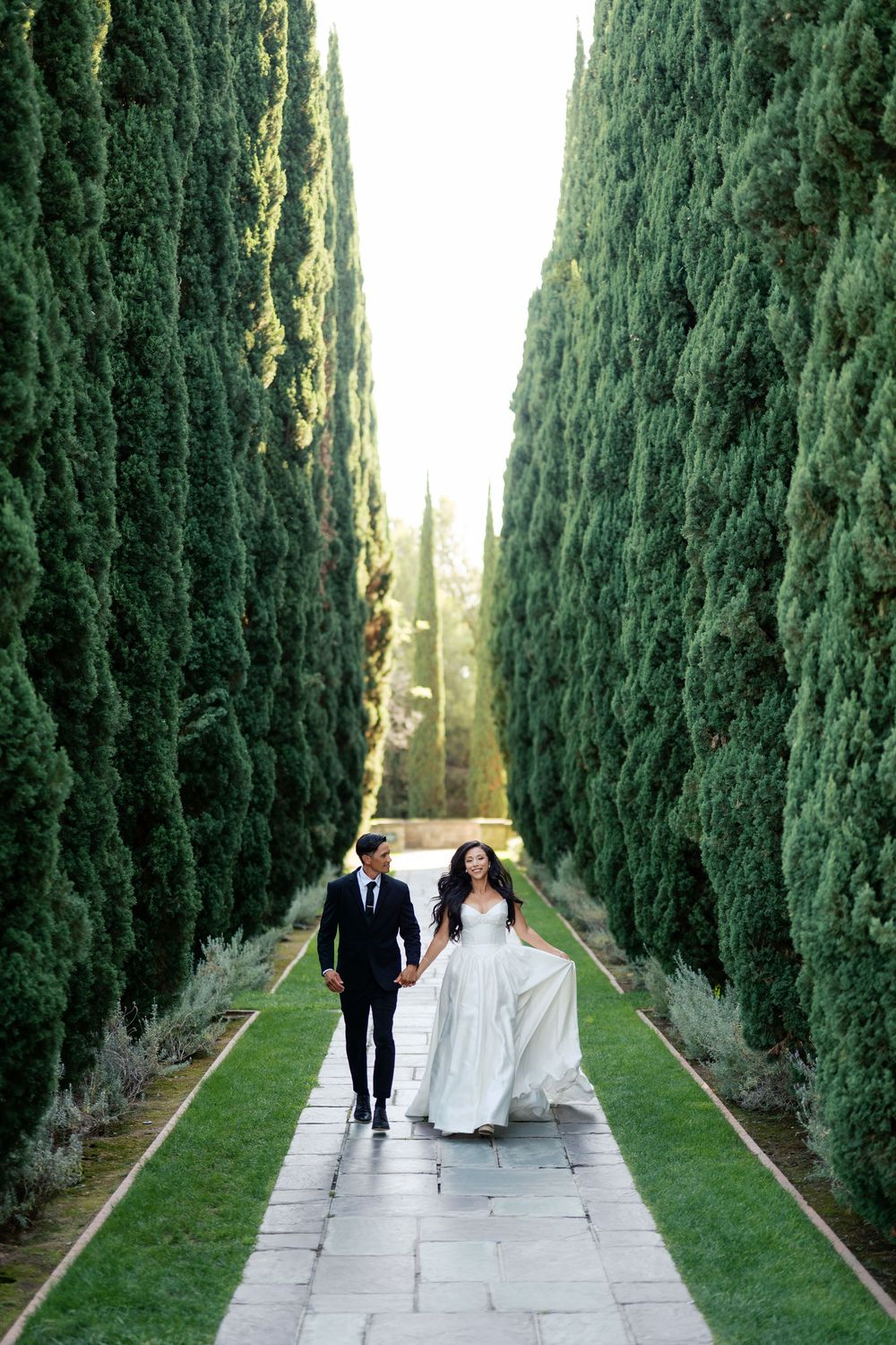 A couple strolls hand in hand down a majestic cypress-lined pathway.