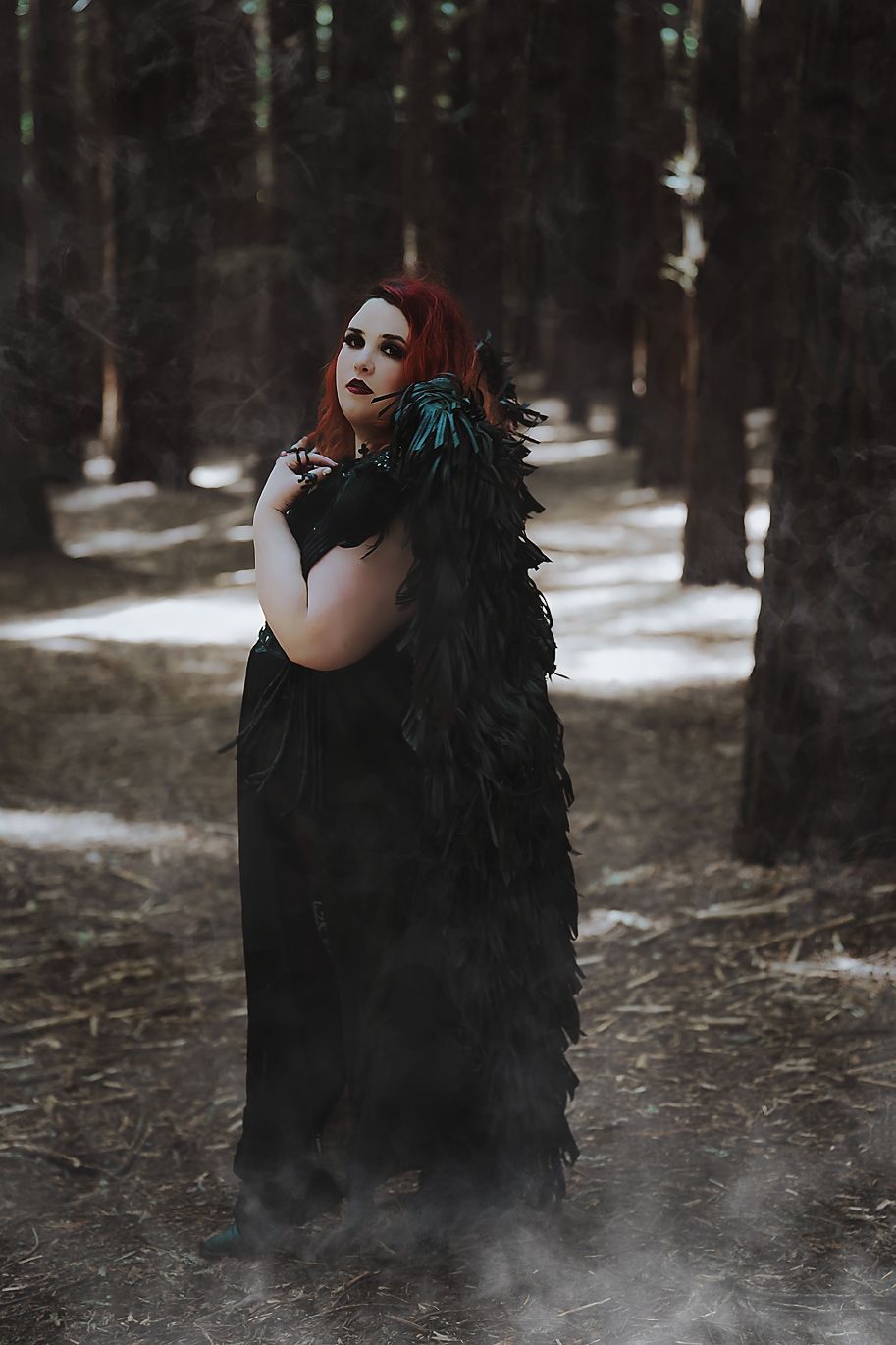 Dark gothic figure in black dress with fog effect stands in snowy forest creating ethereal atmosphere.