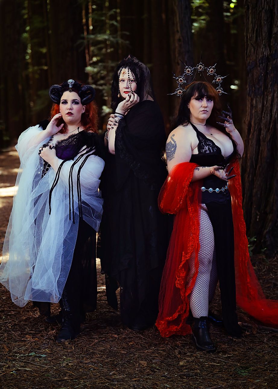 Group dressed in gothic attire poses together in moody woodland setting with dramatic red and black clothing.
