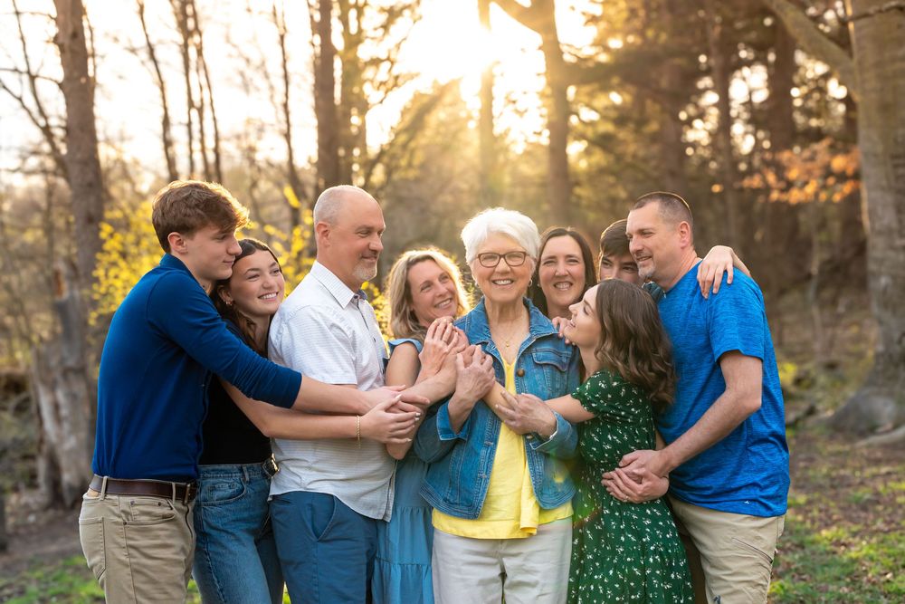 A multi-generational family laughing together outdoors during golden hour in a wooded setting.