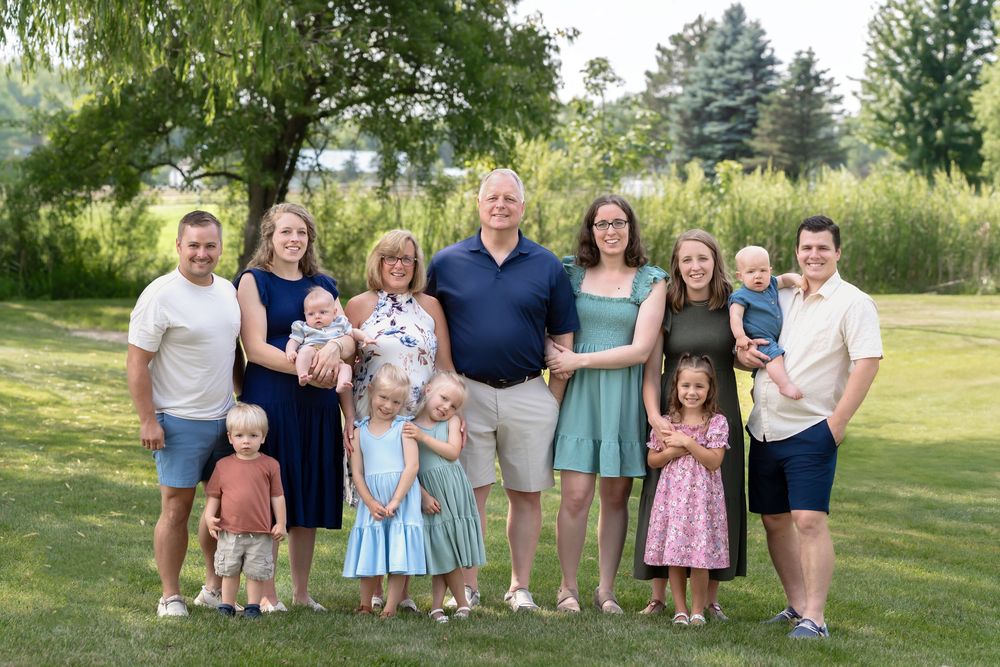 Group of people gathered outdoors on sunny day wearing casual attire standing in a grassy field.