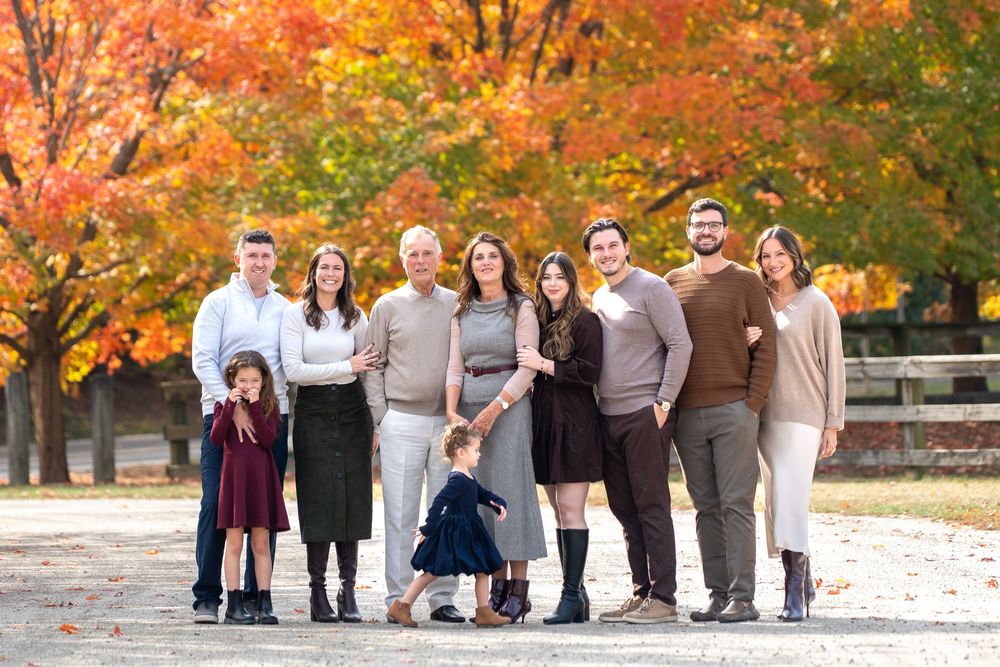 A group stands together outdoors against vibrant orange and red autumn foliage during a fall photo session.