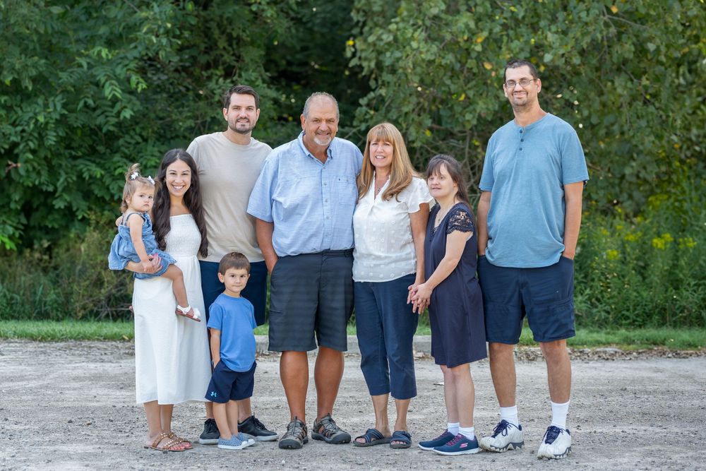Group of casually dressed people standing together outdoors against green foliage background.