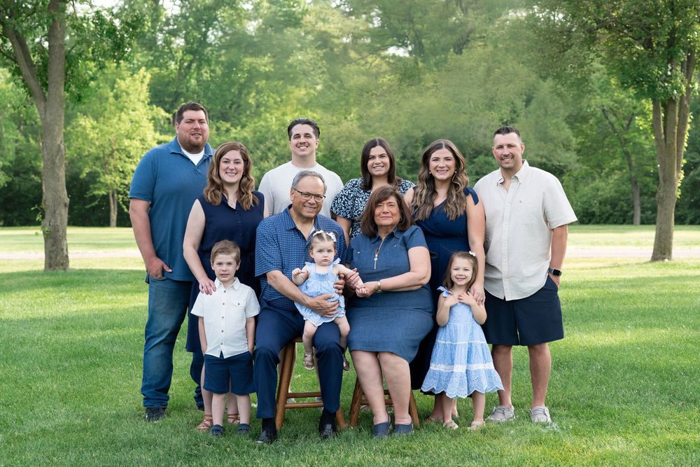 A group of eleven people gathered outdoors for a casual family portrait on a sunny day in a grassy park setting.
