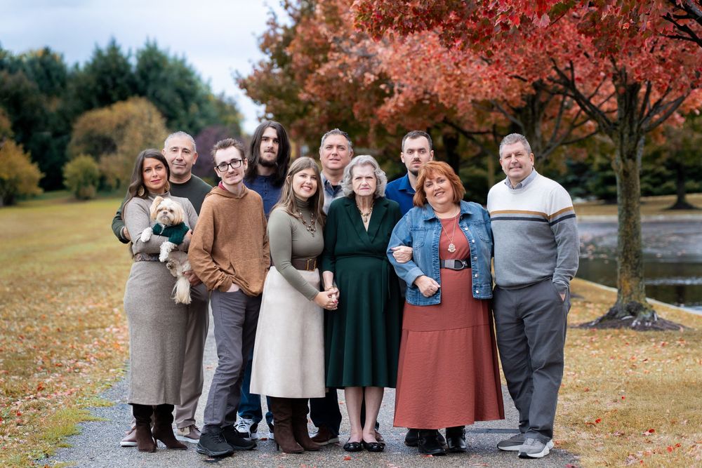 A group gathers for outdoor autumn photos with vibrant red maple trees in the background.