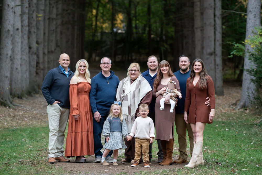 A group of people in coordinated fall outfits pose together outdoors for family photos on a grassy lawn.