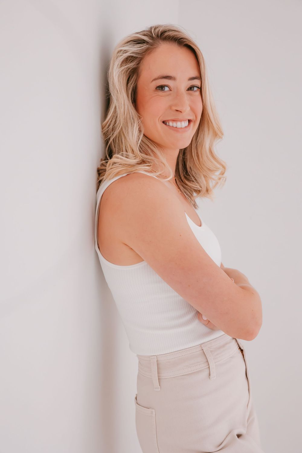 Side profile portrait in white tank top and beige pants against neutral background.