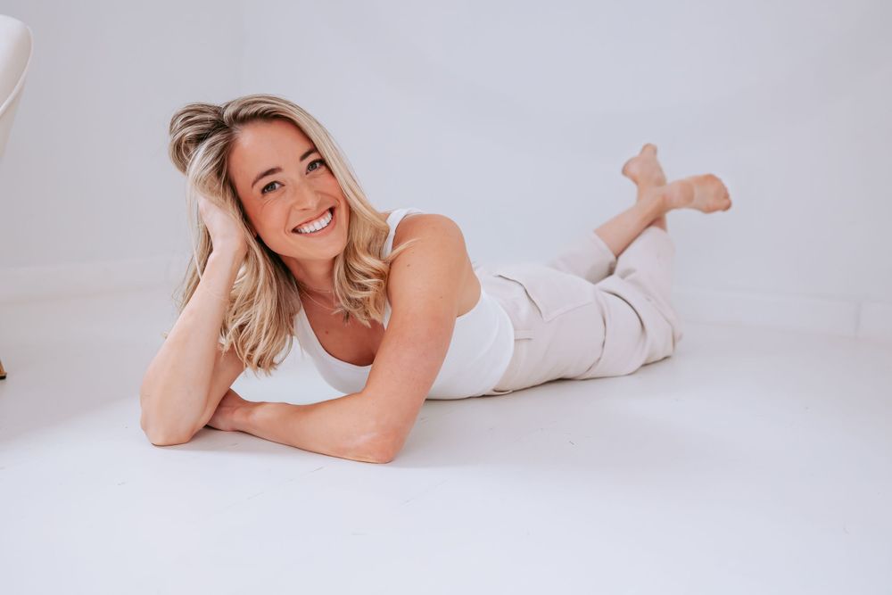 Relaxed full body pose lying on white floor in casual cream colored outfit.