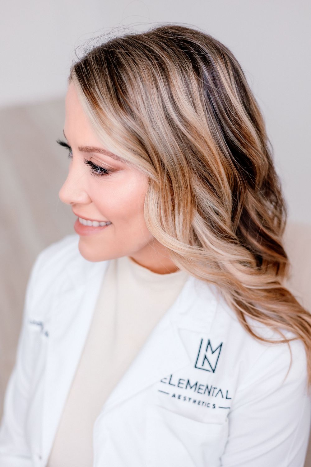 Side profile portrait wearing white medical coat with branded logo against neutral background.