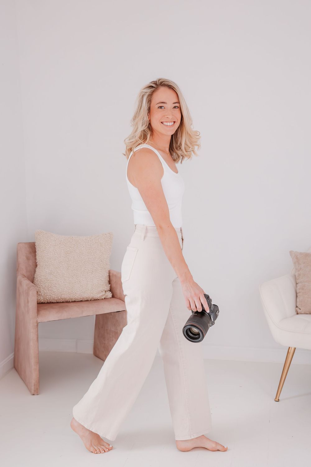Casual lifestyle photo showing photographer holding camera in minimalist studio setting.