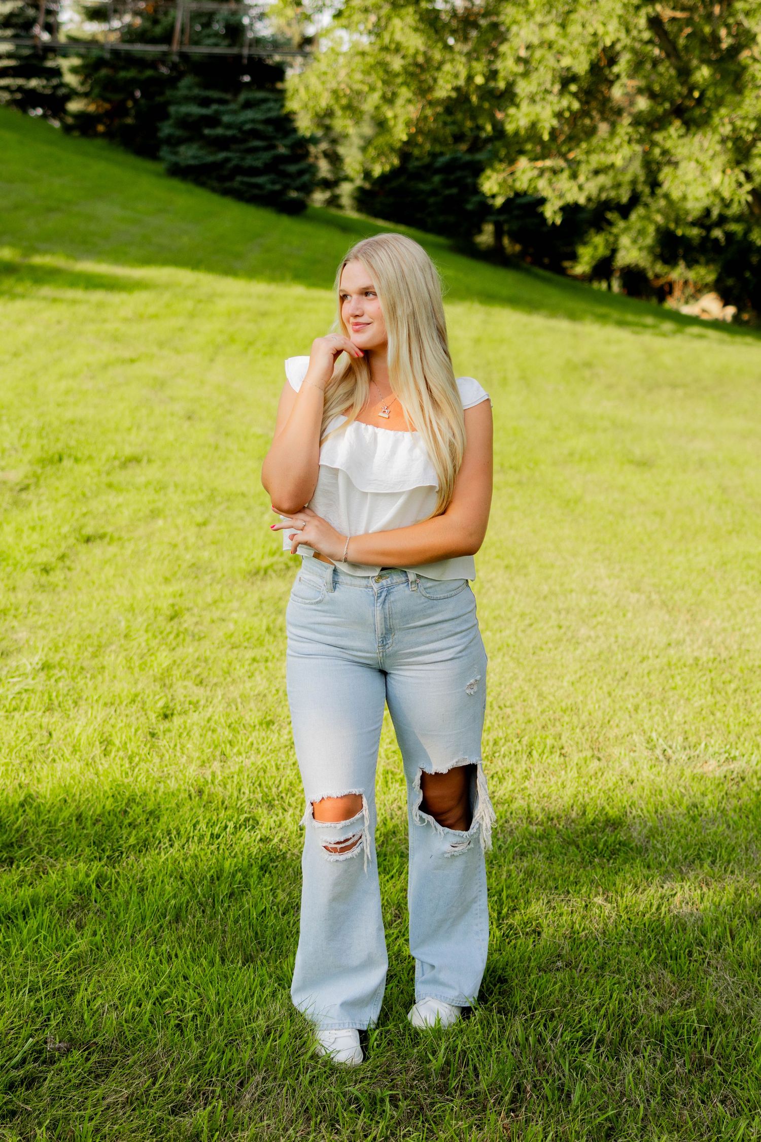 Person wearing light colored top and ripped jeans sitting on grass in a sunny outdoor setting.