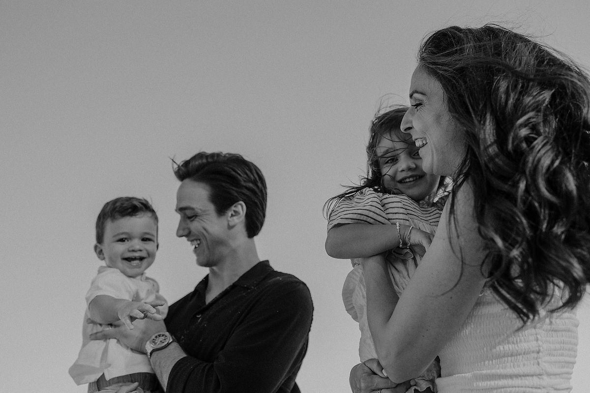 Black and white family photo of parents holding two young children, smiling outdoors against a clear sky.